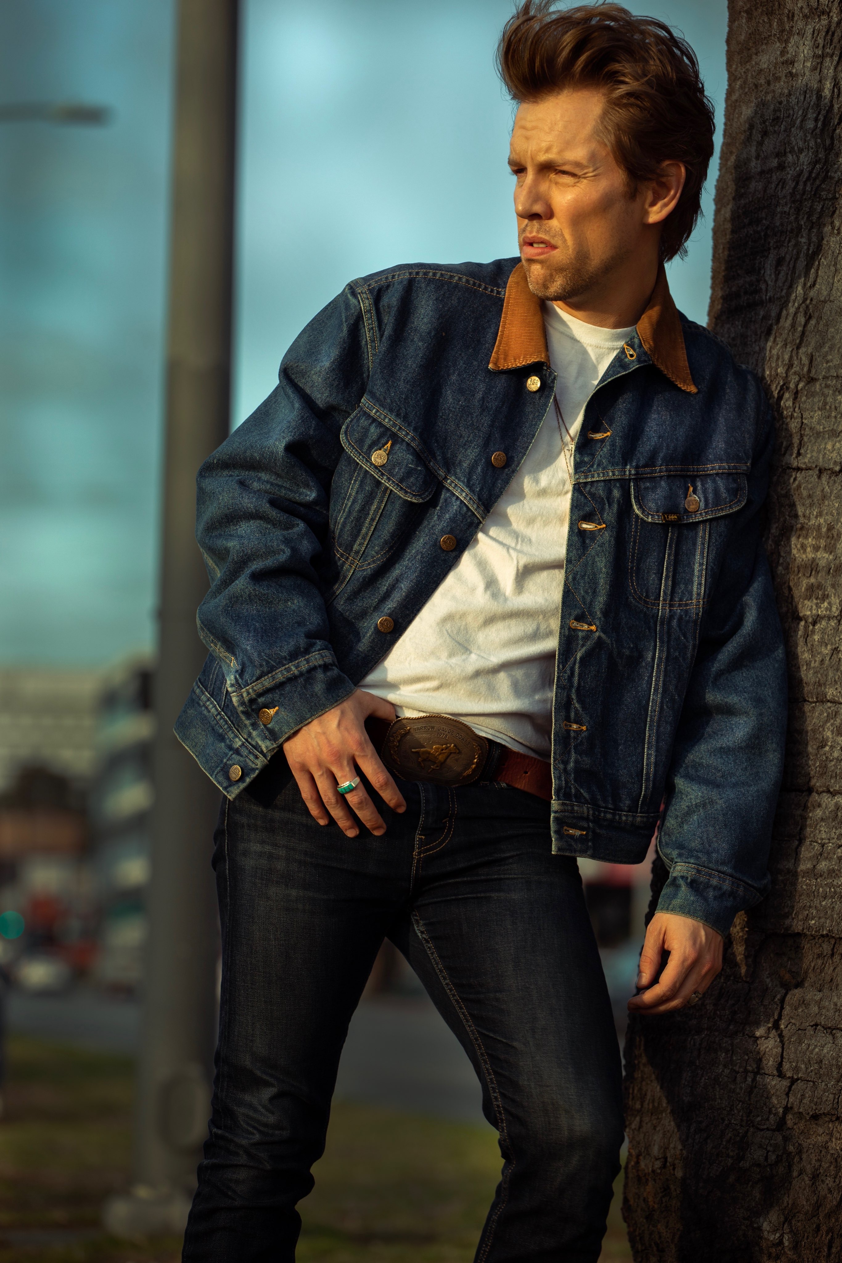 Shawn-Caulin Young in a denim jacket, leaning against a palm tree in warm afternoon light